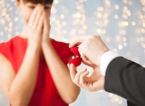 Close up of happy woman and man with engagement ring in gift box over lights background